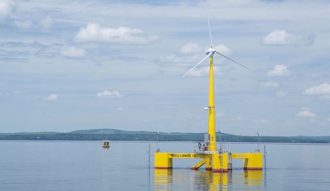 White wind turbine blades sit atop a yellow floating platform in the calm bay