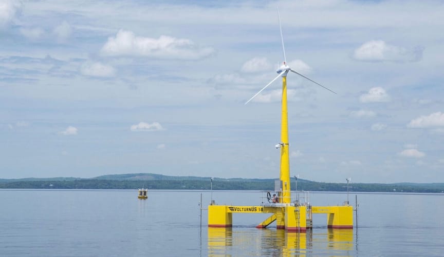 White wind turbine blades sit atop a yellow floating platform in the calm bay