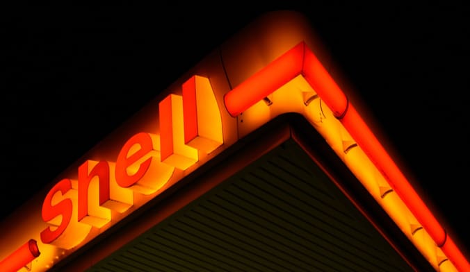 A Shell gas station neon sign lit up in orange at night