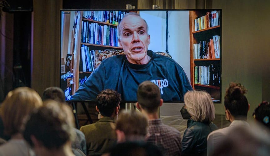 Bill McKibben on a screen in front of a small seated crowd