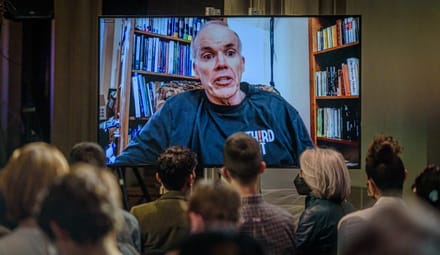 Bill McKibben on a screen in front of a small seated crowd