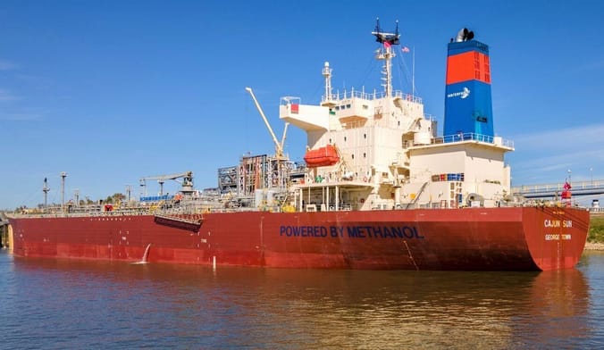A red tanker vessel floats in the water near the shore.