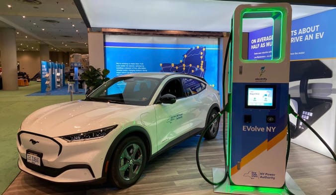 A white electric sedan is parked next to an electric-vehicle charging station with neon green lights