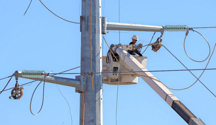 A utility worker in a cherrypicker performs upgrades on high-voltage transmission lines