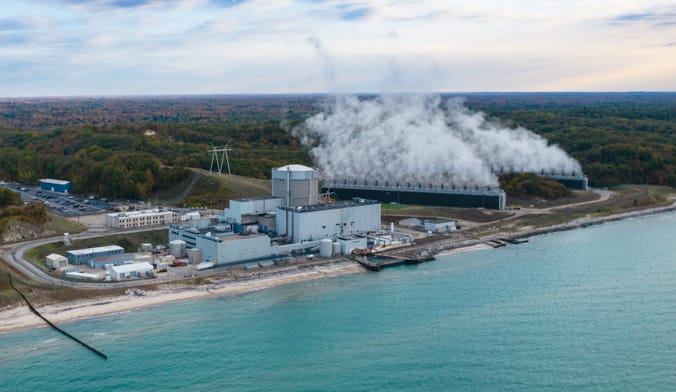 A large industrial facility emitting large clouds of steam sits on the back of a vibrant blue lake
