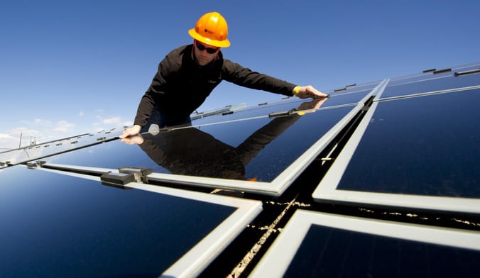 A worker in a hard hat installs a solar panel