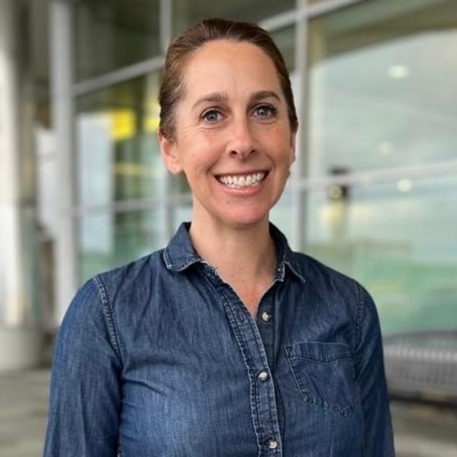 A smiling woman with light skin tone and pulled back hair wearing a denim chambray top
