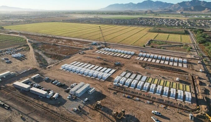 An aerial view of a large construction site with a craggy mountain range in the distance