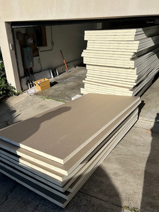Large, flat foam boards with beige sides and white centers are stacked inside and outside of a garage.