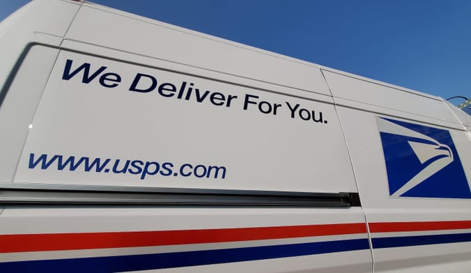 Side of US postal service van with slogan "We deliver for you".