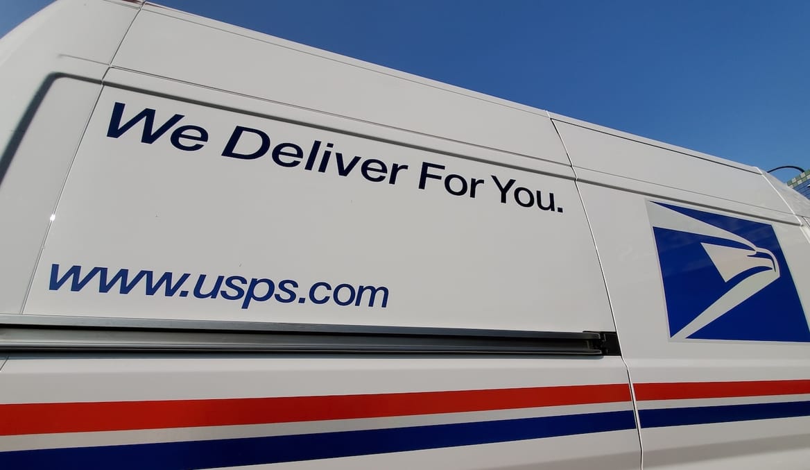 Side of US postal service van with slogan "We deliver for you".