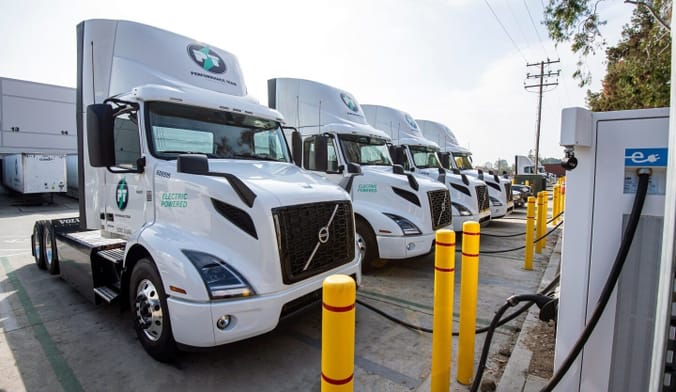 A row of white semitrucks connected to EV chargers
