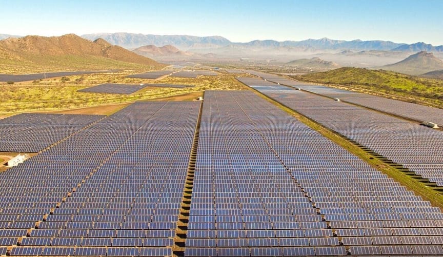 hundreds of black solar panels in an array in a valley surrounded by mountains