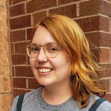 A woman with a light skin tone, shoulder-length reddish hair and glasses