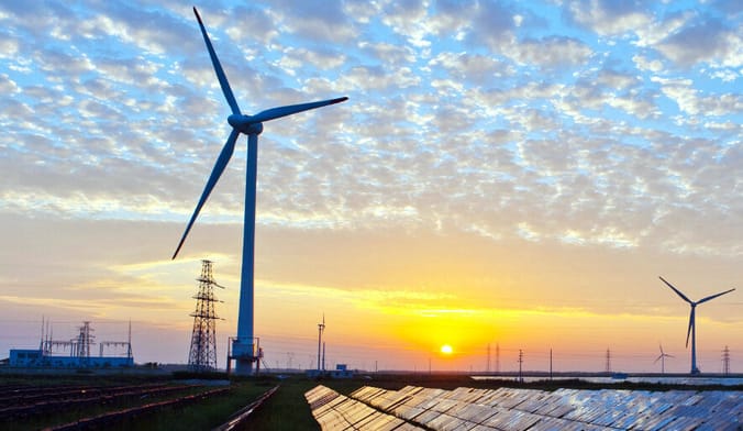 A solar array and wind turbines at sunset