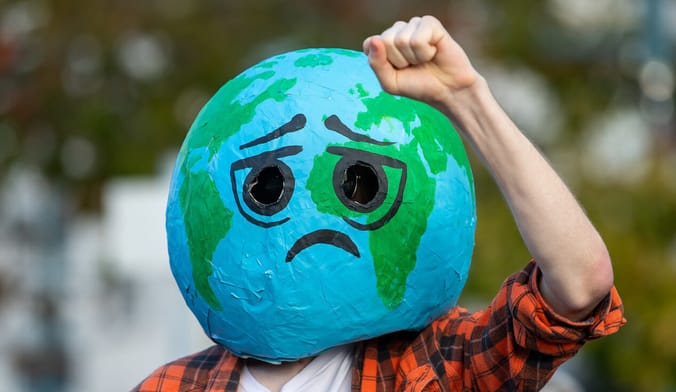 A person wearing a large sad earth mask raises a defiant fist