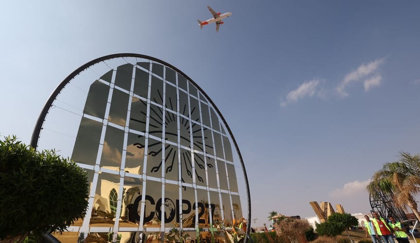 An airplane flies over a large sign that says COP27