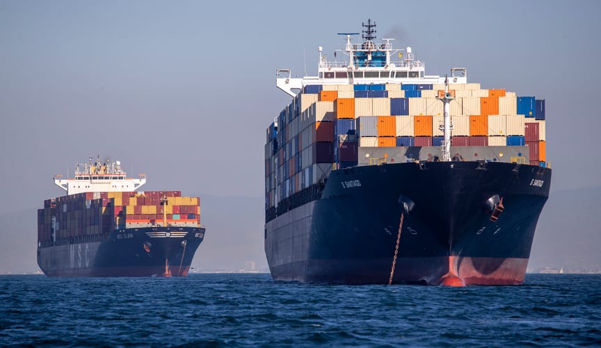 Two cargo ships in the ocean piled high with colorful cargo containers