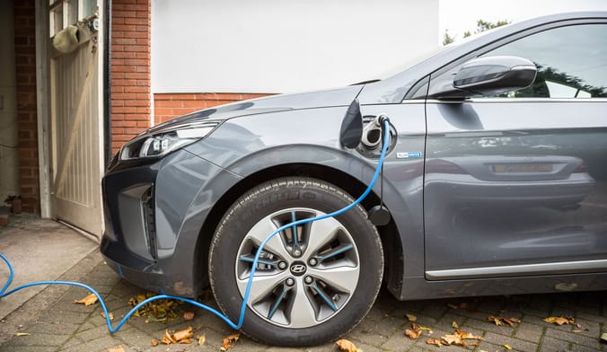A gray electric vehicle plugged into a home EV charger in front of a garage