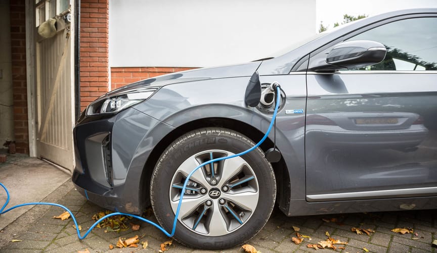 A gray electric vehicle plugged into a home EV charger in front of a garage