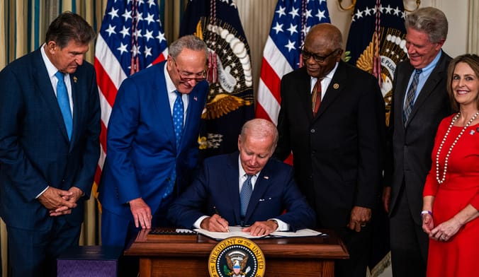 A group of lawmakers look on as President Biden signs a document