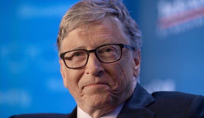 A white man with gray hair and black glasses against a blue backdrop