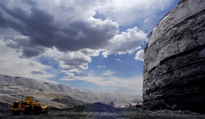 A large black cliff near a valley with excavating equipment under a blue sky with white fluffy clouds