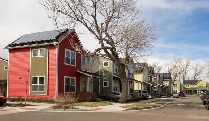 a neighborhood of modest two-story houses with solar panels on their roofs