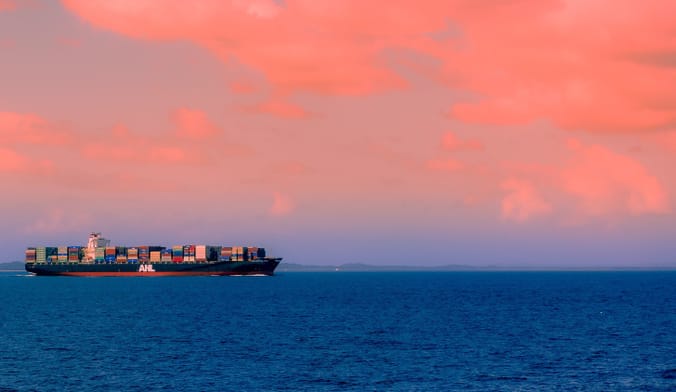 A large cargo container ship sails in the ocean at sunset