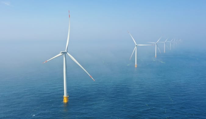 a long line of large white wind turbines in the ocean
