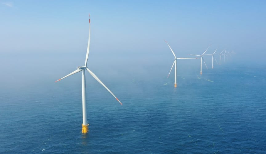 a long line of large white wind turbines in the ocean