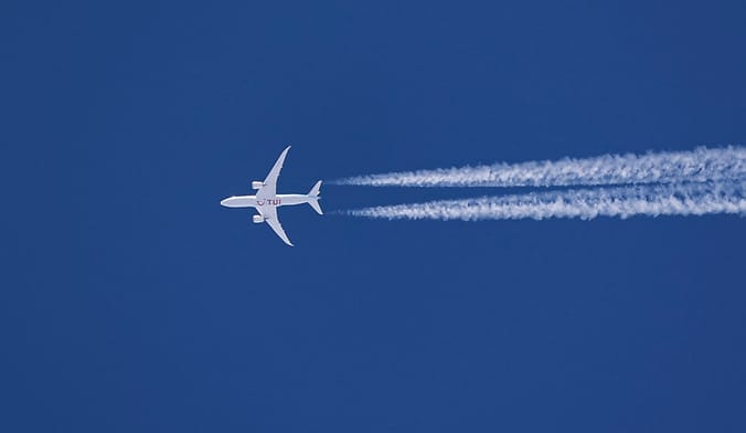 a white airplane flying in the blue sky with contrails streaming out behind it