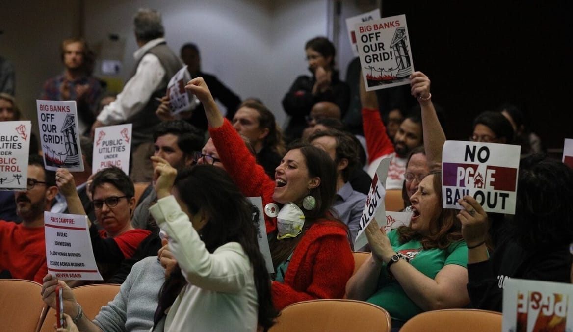 Members of the audience hold protest signs in a meeting room
