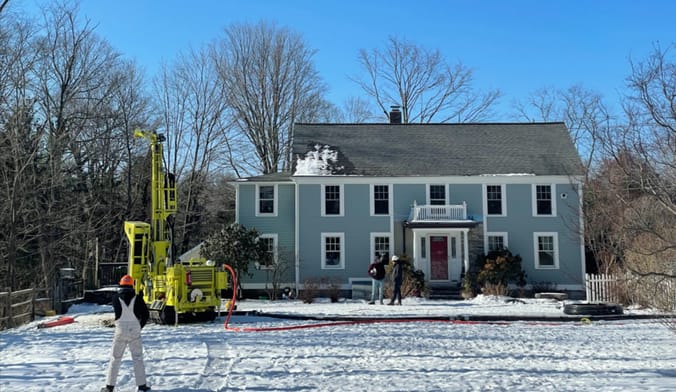 A large drilling rig in front of a two-story blue house