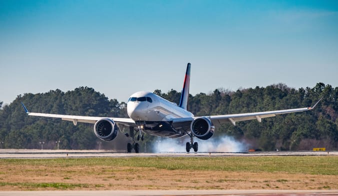 A white airplane takes off from a runway spewing clouds of fumes