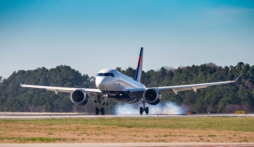A white airplane takes off from a runway spewing clouds of fumes