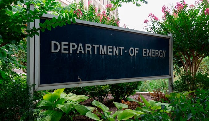 A large black sign with the words Department of Energy surrounding by plants and flowers