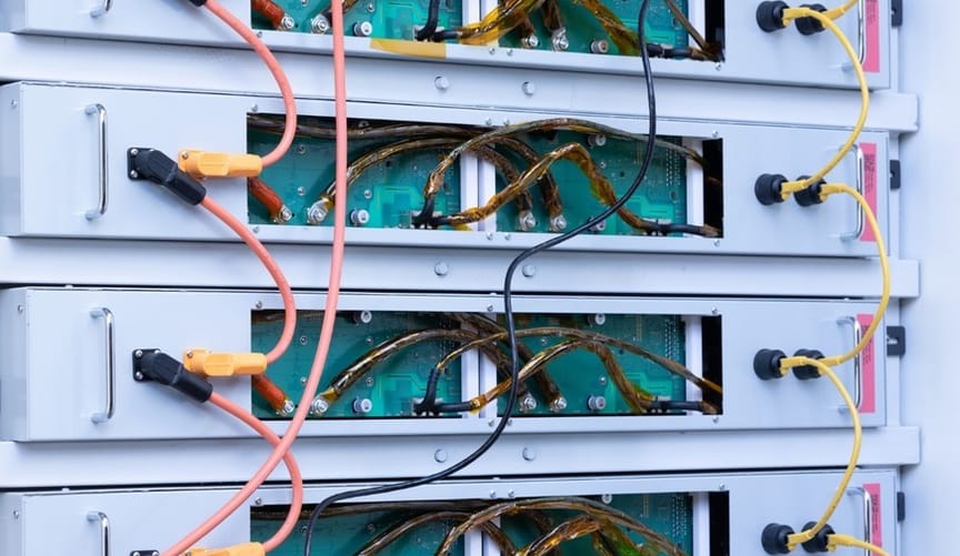 A stack of gray rectangular electronic devices with wiring exposed at the back panel