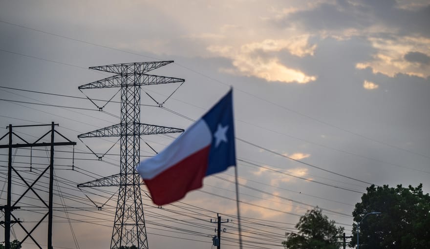A Texas flag flies in front of high-voltage power transmission lines and a blue sky