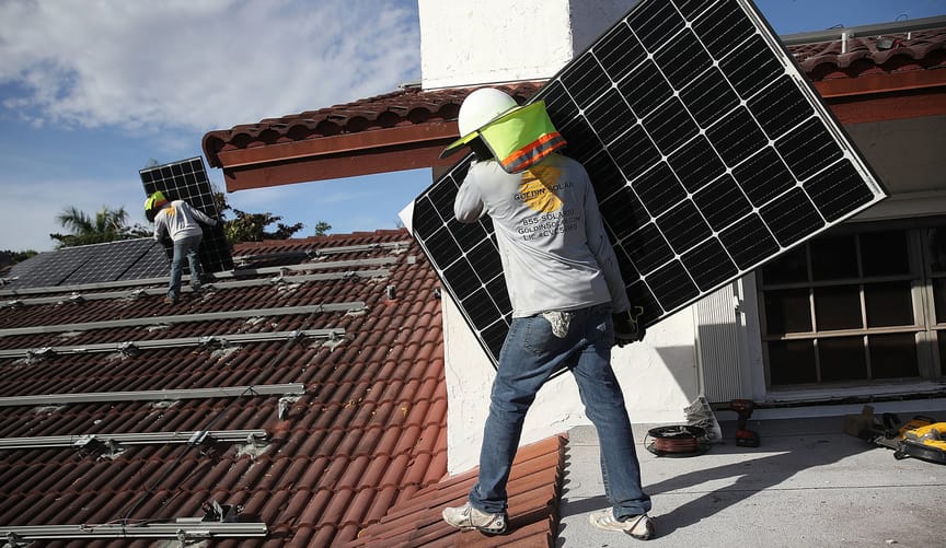 A worker holds a solar panel on the red clay tile roof of a home in Florida
