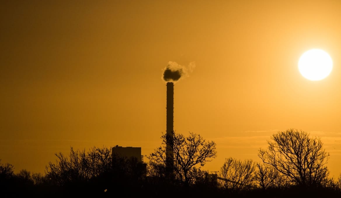 A coal plant spews fumes against the backdrop of an orange sunset