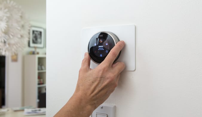a hand adjusting a nest thermostat on the wall