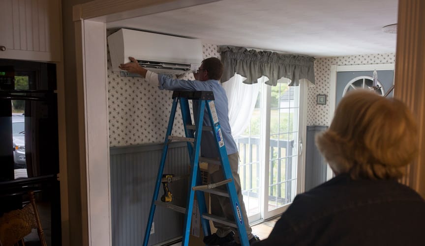 A woman watches as a man installs a heat pump in her home