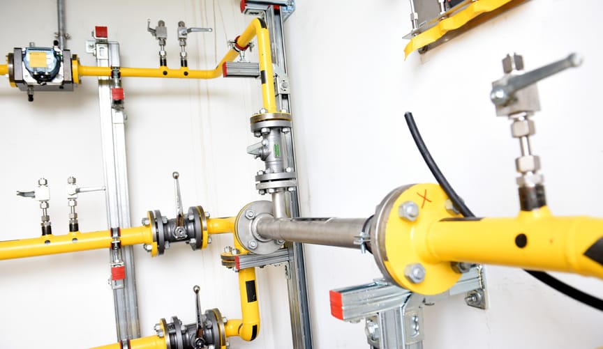 A series of yellow and silver pipes and valves in a white utility room