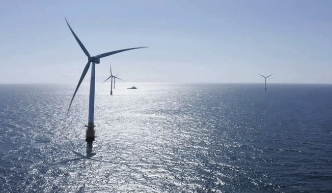 Five white floating wind turbines in the ocean. A boat is seen in the distance.