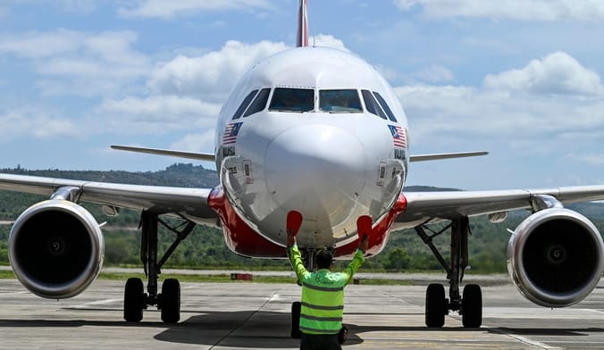 An aircraft marshaller in a green safety vest signals to the pilot of a passenger jet