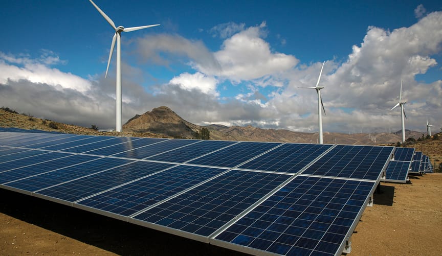 Solar panels and wind turbines against a backdrop of mountainous terrain and an expanse of blue sky