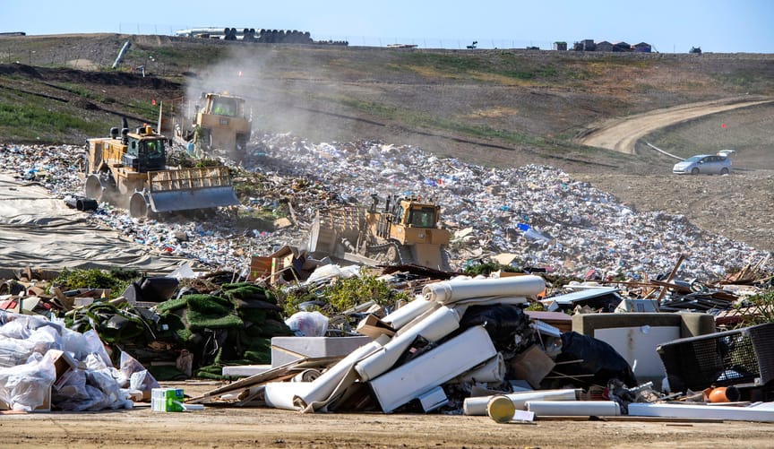 tractors move trash in a large landfill