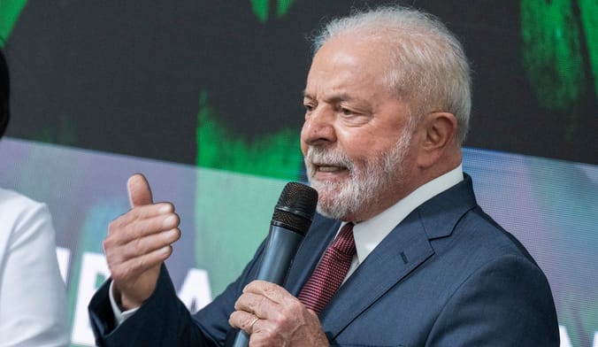A man with white hair and beard wearing a dark blue suit speaks into a microphone