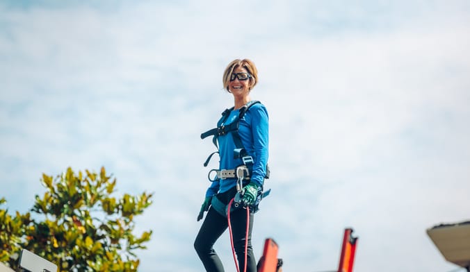 a woman wearing a blue shirt and safety gear stands on a rooftop